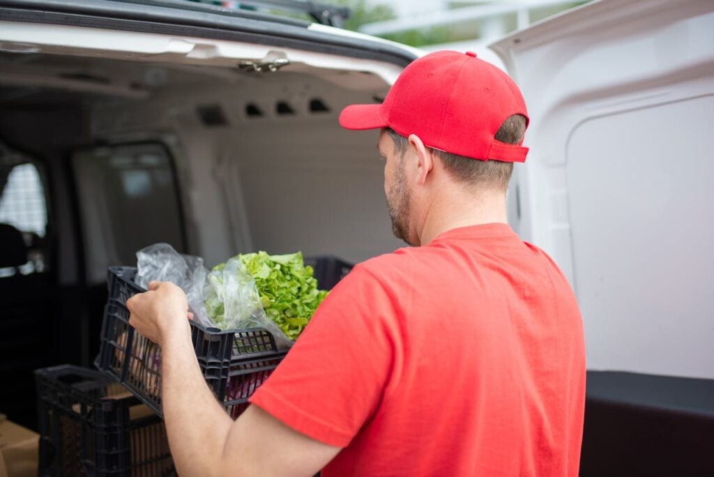 Delivery worker loading produce crates into a van.