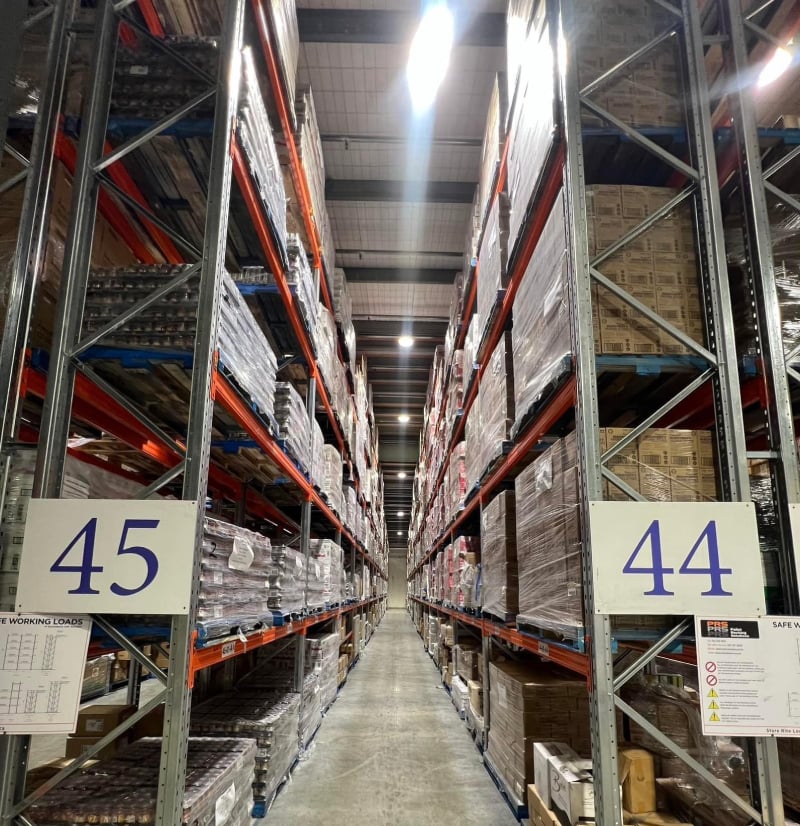 Warehouse aisle with stacked pallets between tall shelving, marked 44 and 45.